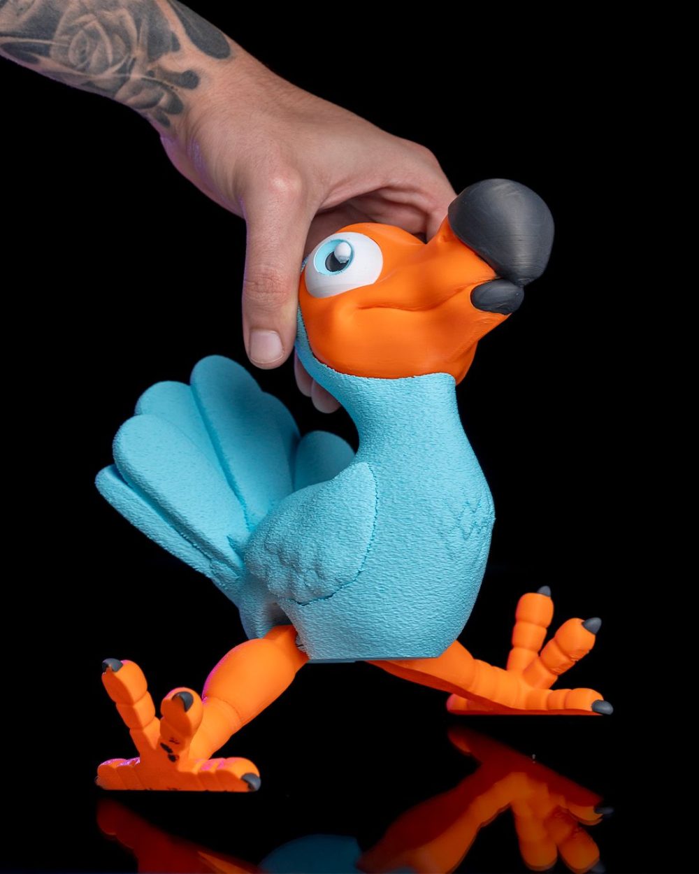 Articulated Dodo Bird – Custom – 3D Printed – Figure in blue and orange, held by a hand against black background.