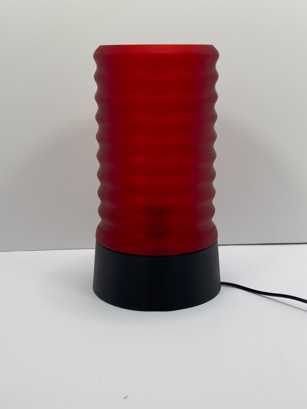 The Wavy Table Lamp with a red, textured cylindrical shade on a black base, displayed against a plain background.