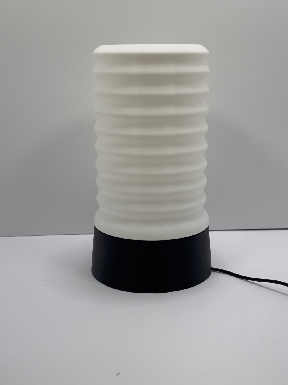 The Wavy Table Lamp features a white, wavy cylindrical design atop a black base, perfect for modern and stylish interiors.