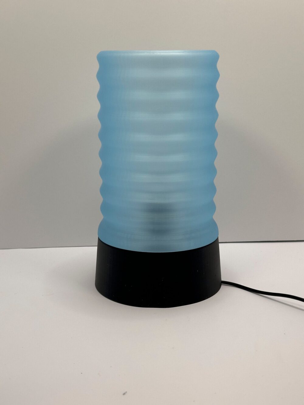 The Wavy Table Lamp, featuring a blue glass shade with wave patterns and a black base, perfect for modern home decor.