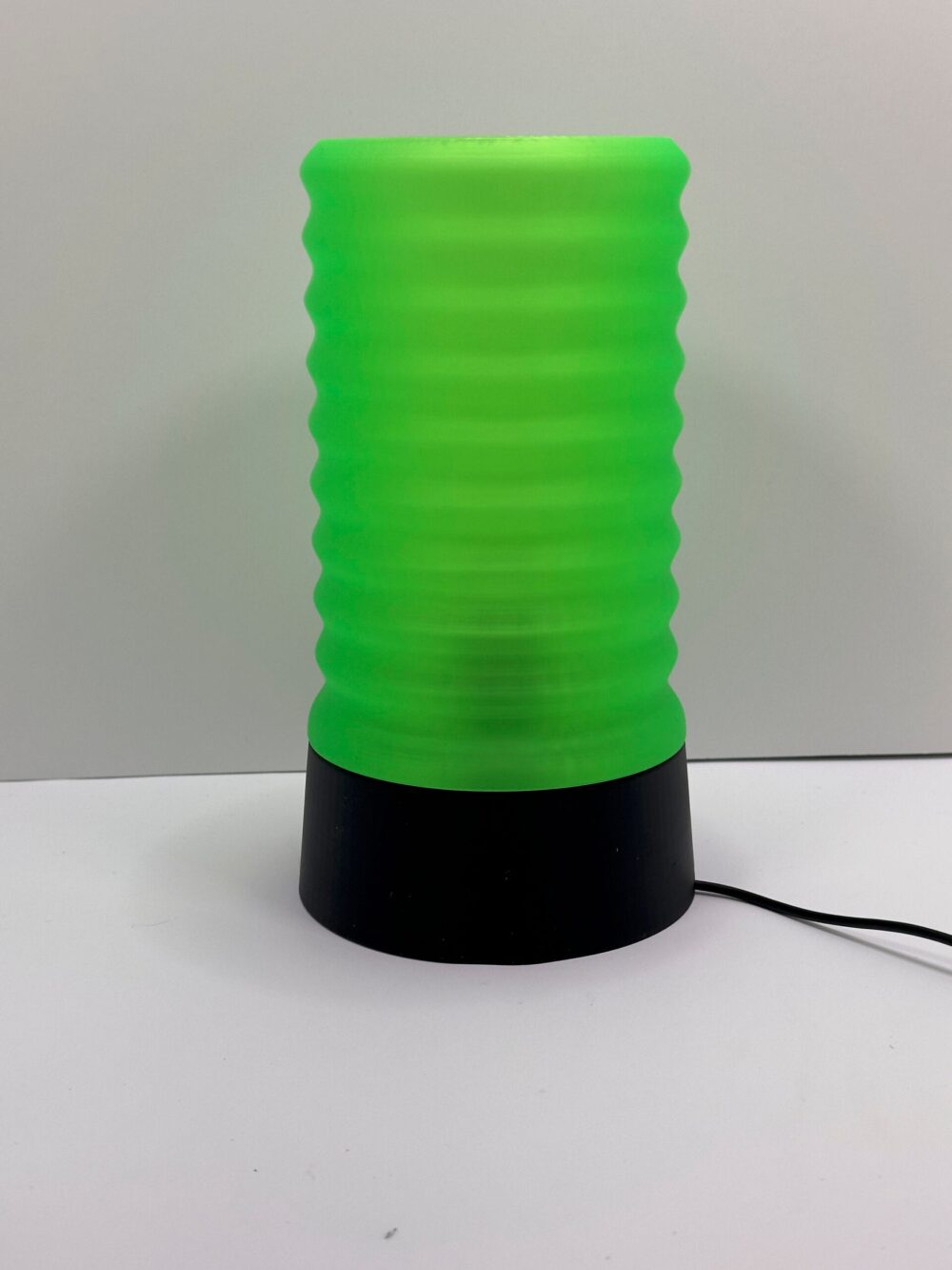 The Wavy Table Lamp features a vibrant green, wavy-textured cylinder shade atop a sleek black base.