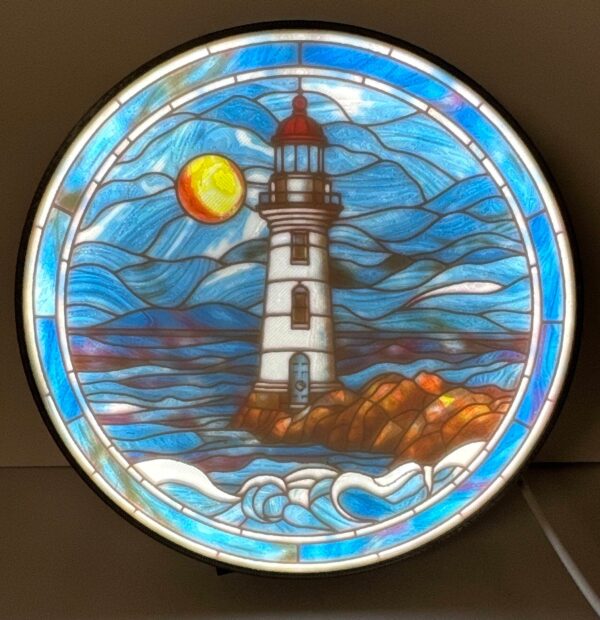 Stained glass lithophane decoration of a lighthouse with a bright sun and ocean waves, displayed against a dark background.