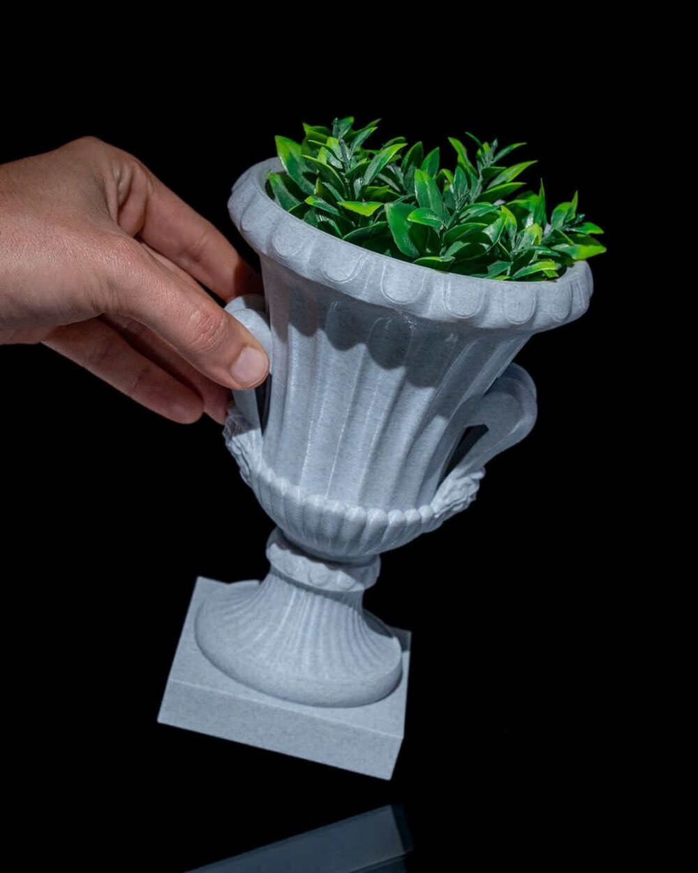 Hand holding an Elegant Roman Cup Planter with green foliage, showing its Greco-Roman style and intricate details on a black background.