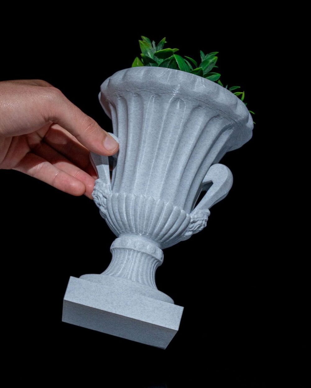 Hand holding an Elegant Roman Cup Planter with green plants, showcasing its Greco-Roman design and antique style on a black background.